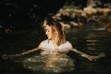 Fototapeta premium A woman immersed in clear water with a nature background, exuding a serene and contemplative mood. Perfect for themes of tranquility, relaxation, and natural beauty.