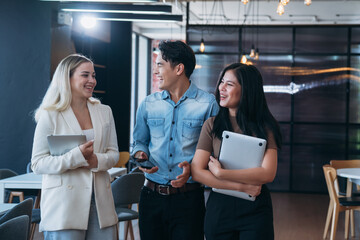 Three people are walking together in a room, smiling and holding laptops