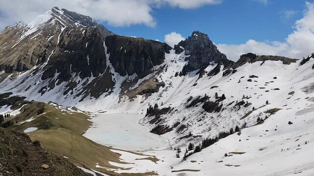 Hd video of Lessy lake in spring, with mountains covered in snow and ice recovering the alpine lake in Haute Savoie, in massif of Bornes Aravis