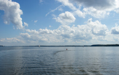 A serene lake scene with sailboats gliding on calm waters and fluffy clouds scattered in a bright blue sky. Ideal for nature and outdoor themes.
