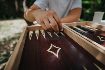 A close-up view of a person playing backgammon outdoors on a sunny day. The image highlights hand movements and strategic game play.