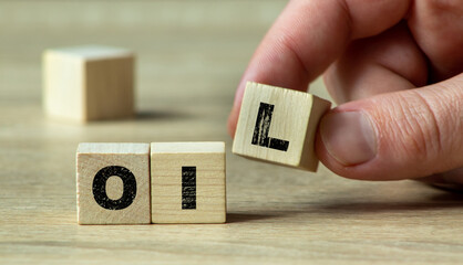 Wooden cubes spelling "OIL" with hand changing to "LOL," on wooden surface. Concept of humor, wordplay, and language.