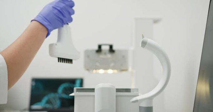 Scientist using laboratory equipment in modern research facility. Gloved hand preparing device for research. High-tech lab setting with computer displaying DNA sequence in background.