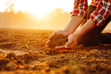 A farmer examines soil quality at sunset while kneeling in a sunlit field, showcasing a connection...