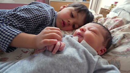 Young boy lying on the bed next to newborn sibling, smiling with joy, highlighting the pure...