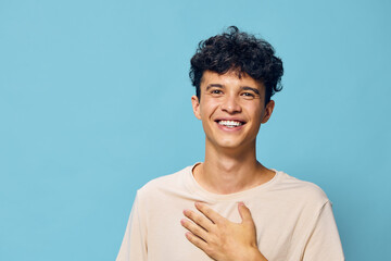 Smiling young man with curly hair on a pastel blue background, expressing happiness and warmth His casual beige shirt complements the cheerful vibe of the image