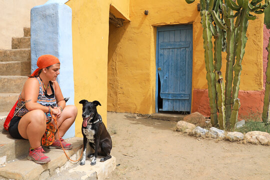 mujer joven turista con perro negro sentados en las calles de un pueblo con paredes pintadas de color y con cactus mexico almer&iacute;a cabo de gata 4M0A6044-05