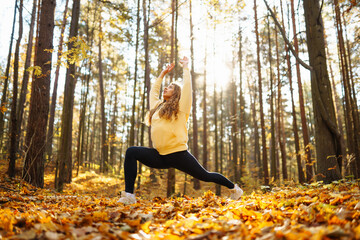 A serene woman practices yoga meditation in a sunlit forest surrounded by autumn leaves. Lifestyle and Meditation concept.