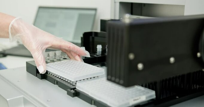 Laboratory technician wearing gloves placing microplate into automated machine for scientific analysis. Modern laboratory setup for accurate research and development.