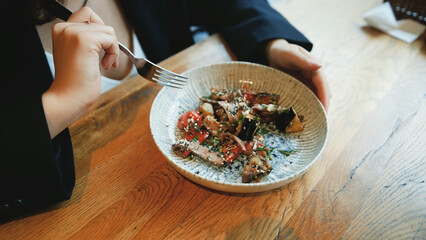 Dinner at a restaurant. A woman eats an eggplant and cheese salad with appetite. Close-up.