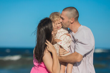 Fototapeta premium Happy family. Parents kiss daughter at the ocean