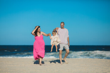 Happy Family swinging and spinning cute daughter in circles by the arms at the beach. Playful, energetic and joyful kid having fun