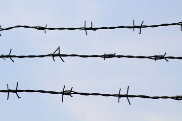 Barbed wire fence against blue sky with white clouds. Barbed wire isolated on a blue background. Barbed wire abstract background