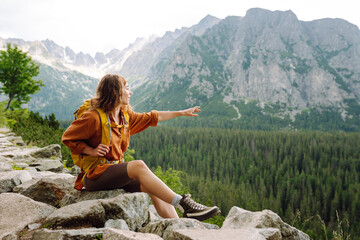 Naklejka premium A hiker enjoys the fresh mountain air while trekking a rocky trail through the lush green landscape in the afternoon light. Concept of an active lifestyle.