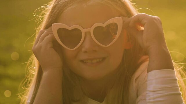 Summer portrait of a cute little girl in a heart sunglasses. Happy childhood concept.