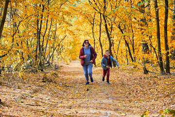 A mother and son are jogging through a vibrant autumn forest, surrounded by golden leaves.