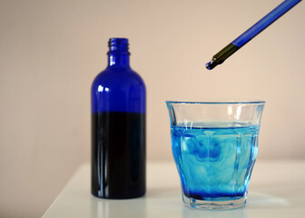 image showing a bottle filled with methylene blue  near a glass with water and methylene blue and a...