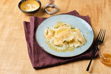 Cooking pumpkin ravioli, ready boiled ravioli, sprinkled with parmesan and drizzled with aromatic rosemary oil, on a gray ceramic plate. Recipes pumpkin.