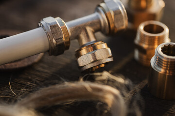 Brass plumbing fittings and PEX pipe fittings lying on an old wooden countertop, next to a tool, plumbing wrenches (selective focus)