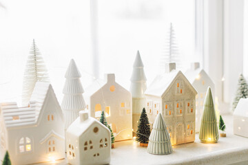 Christmas little ceramic houses, white snowy trees and golden lights on window. Xmas background....
