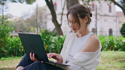 Woman typing laptop park sitting at green grass closeup. Beautiful freelancer