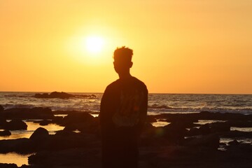 Fototapeta premium Lonely man standing on the beach watching the sunset