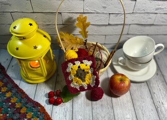 Cozy autumn photo with crocheting, clews of wool, basket, candle light and cups