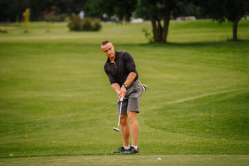 A focused golfer prepares to putt on a green golf course. He wears a black shirt and shorts,...