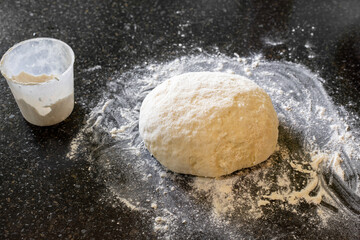 a lump of dough on a black table with scattered flour. Kneaded dough for home baking.