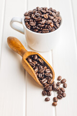 Roasted coffee beans in wooden scoop on white table.