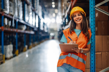 Cheerful female worker records data with clipboard in warehouse.