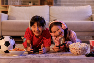 Little children playing video game at home in evening