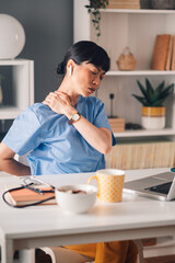 Asian woman ealthcare professional in scrubs massages neck at work desk