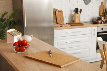 Wooden cutting board with knife and fresh tomatoes on table in modern kitchen