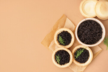 Tasty tartlets with black caviar on beige background