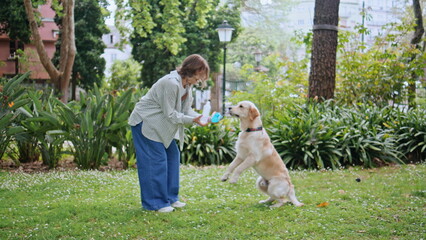 Loving girl playing dog on green nature. Young woman giving water to retriever 