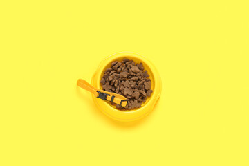 Bowl of dry pet food and collar on yellow background