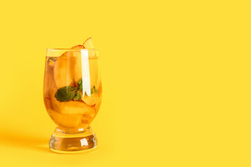 Glass of fresh peach lemonade with mint on yellow background