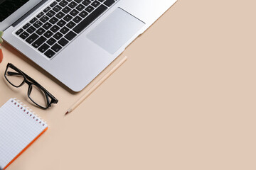 Modern laptop, notebook, pencil and eyeglasses on color background