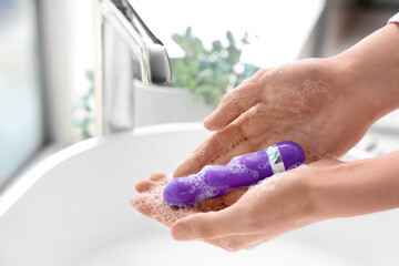 Woman washing vibrator over sink in bathroom, closeup