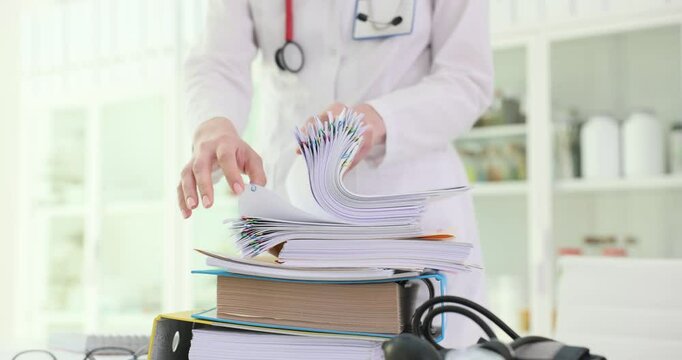 Female hands search for document in stack of papers in hospital room. Woman medic carefully reviews documents looking for necessary patient records