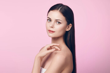Beautiful young woman with long straight hair posing on a pink background, with her hand on her chin and looking at the camera
