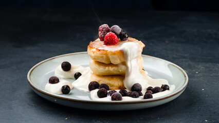 Fresh cheese pancakes with black currant, raspberry and sour cream in a plate.