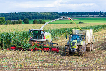 combine harvester and tractor working in a field at maize harvest