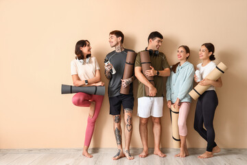 Group of sporty young people with yoga mats near beige wall
