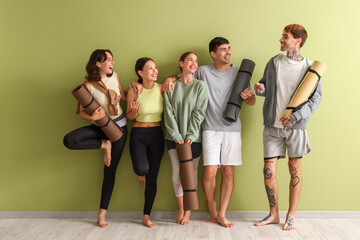 Fototapeta premium Group of sporty young people with yoga mats near green wall