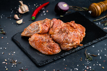 Raw marinated barbecue chicken with spices and salt on a dark background.