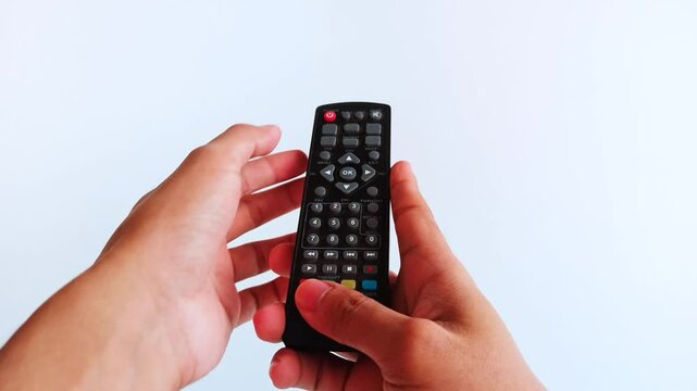 a hand holding a TV remote, with fingers pressing buttons several times