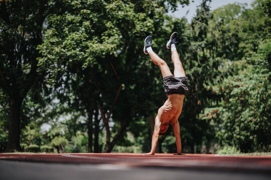 Athletic man in a park performing an impressive handstand on an outdoor track, demonstrating strength, balance, and physical fitness on a sunny day.