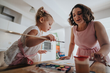A mother and daughter enjoy painting together in a bright kitchen setting. The daughter is focused on her drawing while the mother supervises.